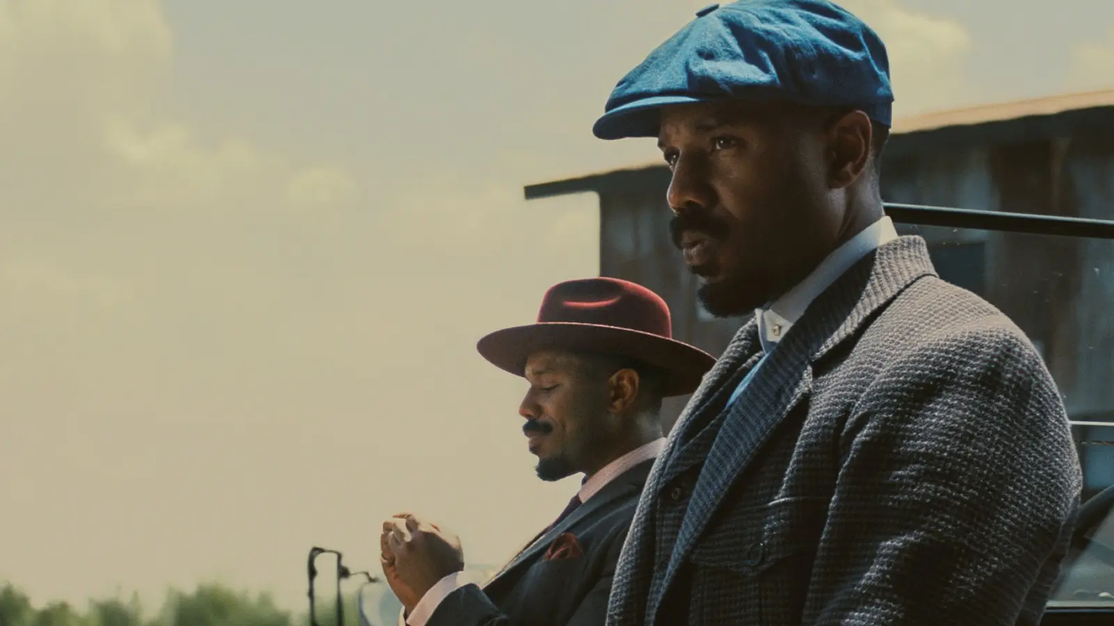 Michael B. Jordan as twins Smoke and Stack in Sinners, showcasing the contrasting blue and red period costumes designed by Ruth E. Carter.