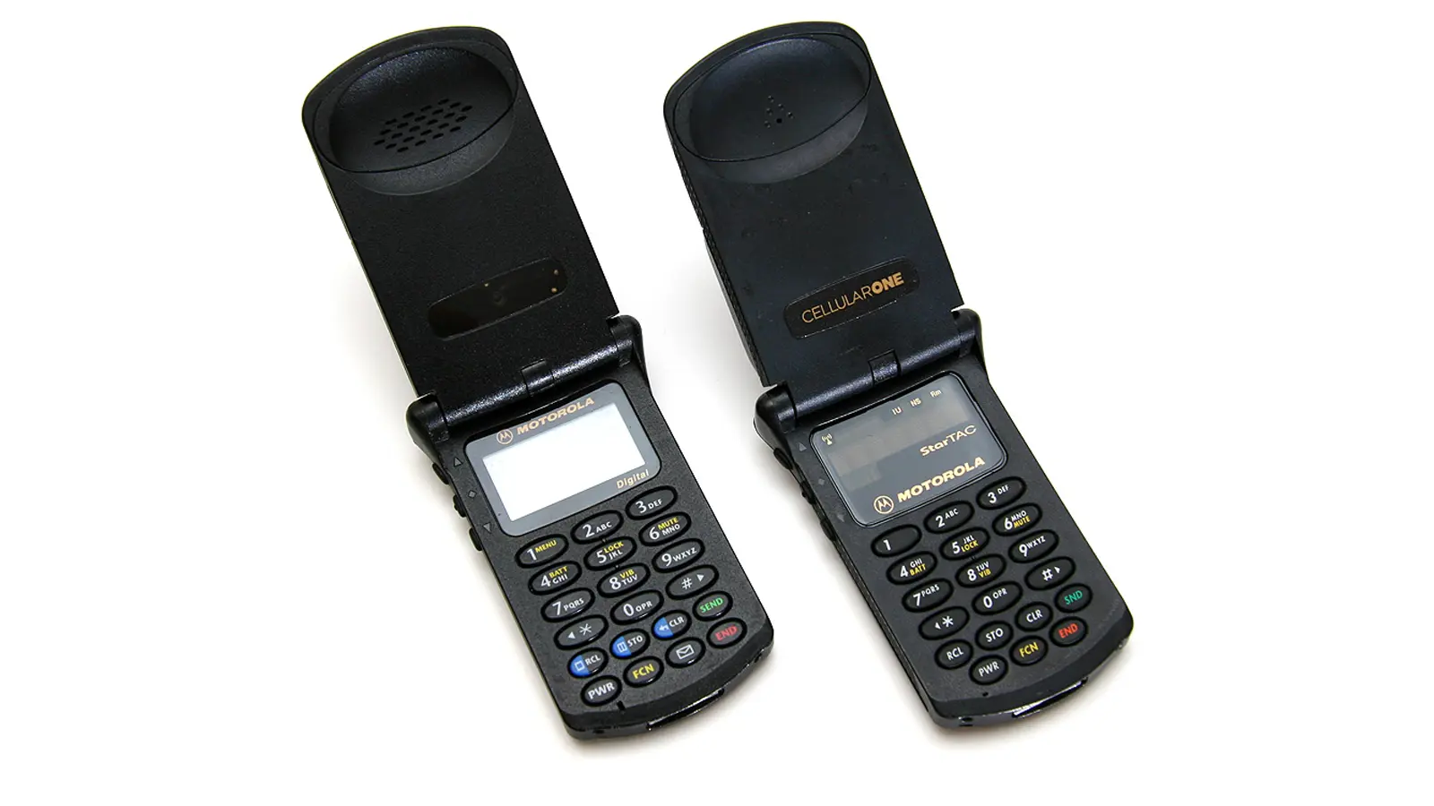 A studio-lit profile view of the 1996 Motorola StarTAC in its open position. The image captures the iconic 45-degree clamshell angle, the vintage red LED dot-matrix display, and the mechanical keypad layout that defined 90s wearable tech.