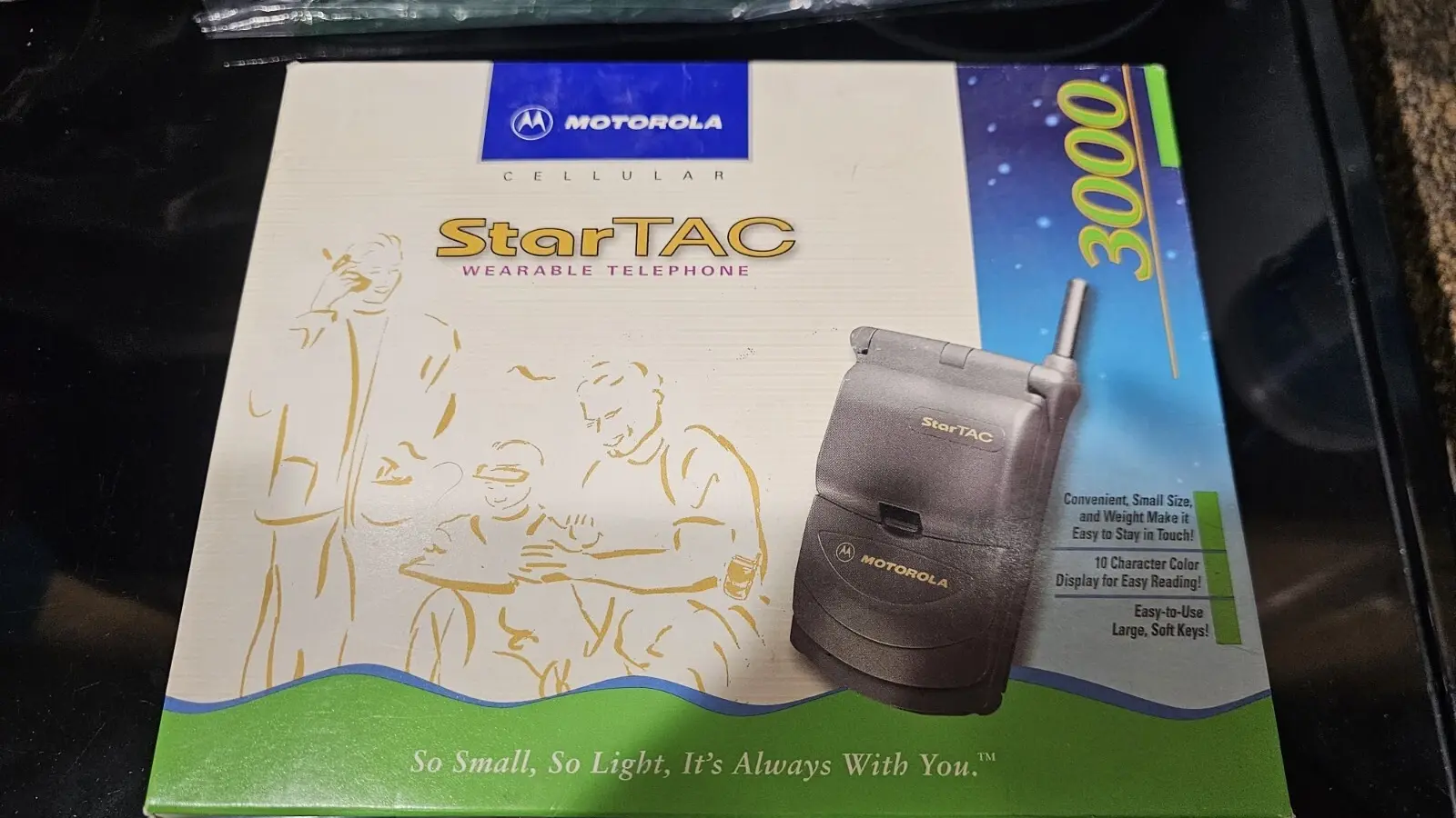 A front-facing view of a refurbished Motorola StarTAC 85 collector's unit. The image shows the device in its closed position, highlighting the compact "wearable" form factor and the iconic Motorola batwing logo on the textured black casing.