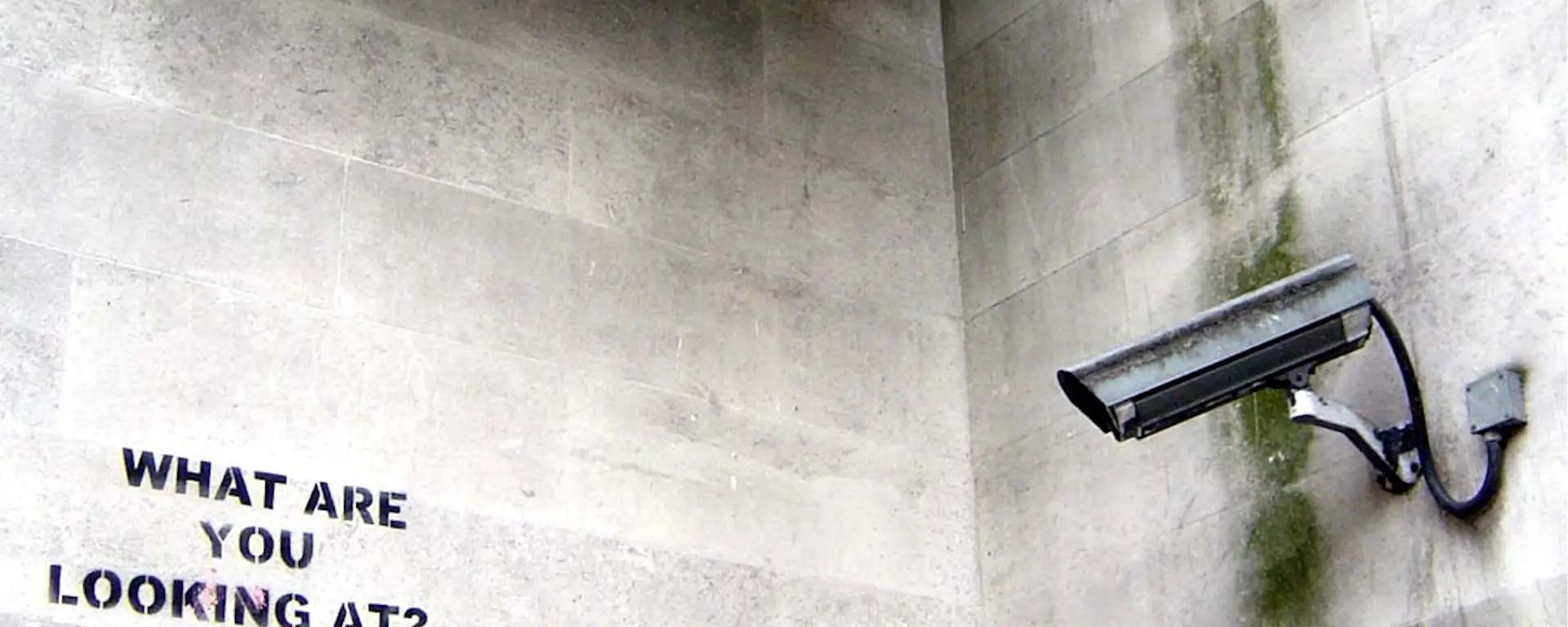 A sleek, high-tech security camera mounted on a city wall, symbolizing the invisible data collection and algorithmic surveillance of urban communities.