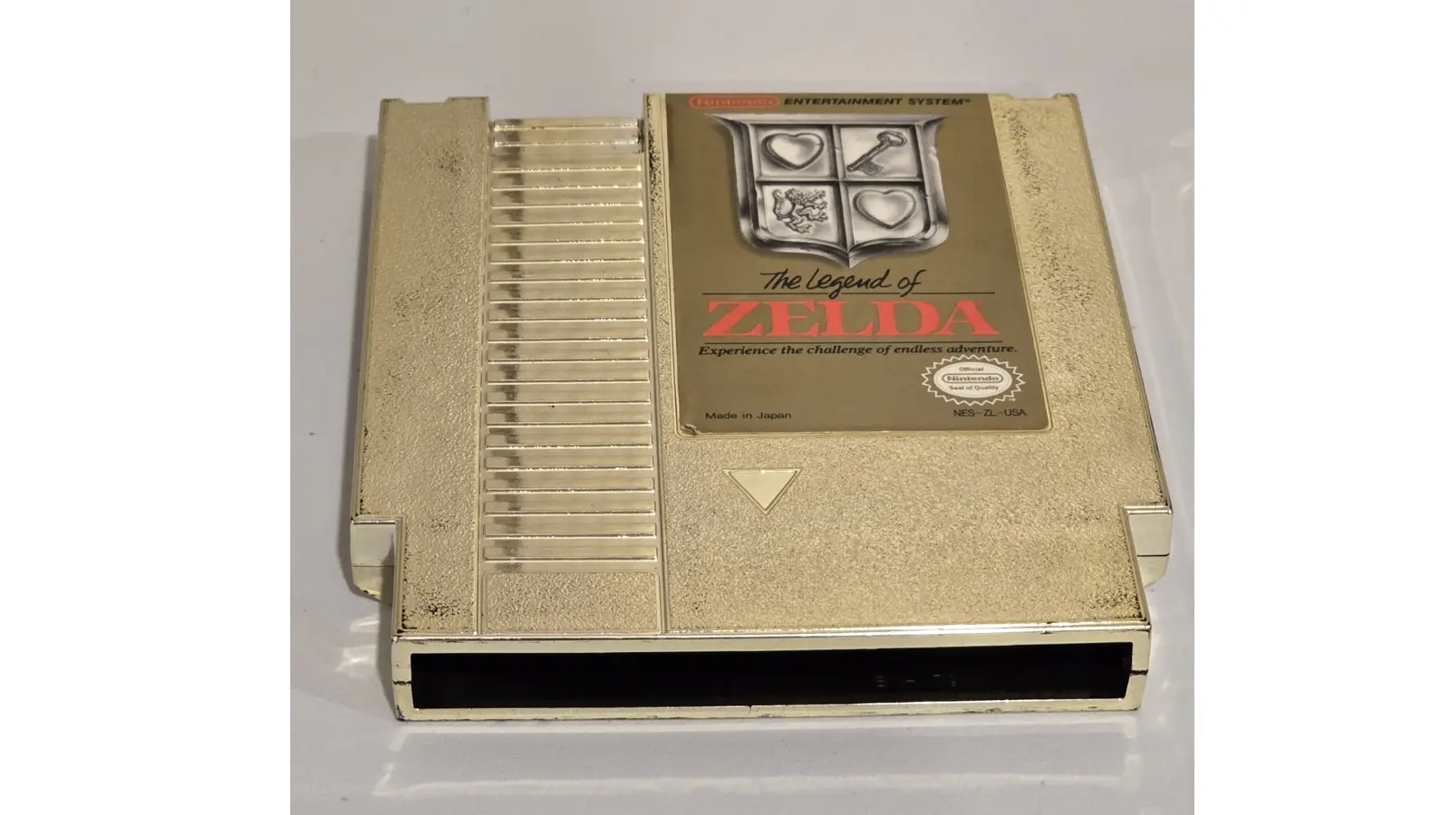 A high-resolution close-up of the 1986 Legend of Zelda gold-plated NES cartridge, showing the metallic reflective finish, the iconic shield logo, and the red Nintendo Seal of Quality.