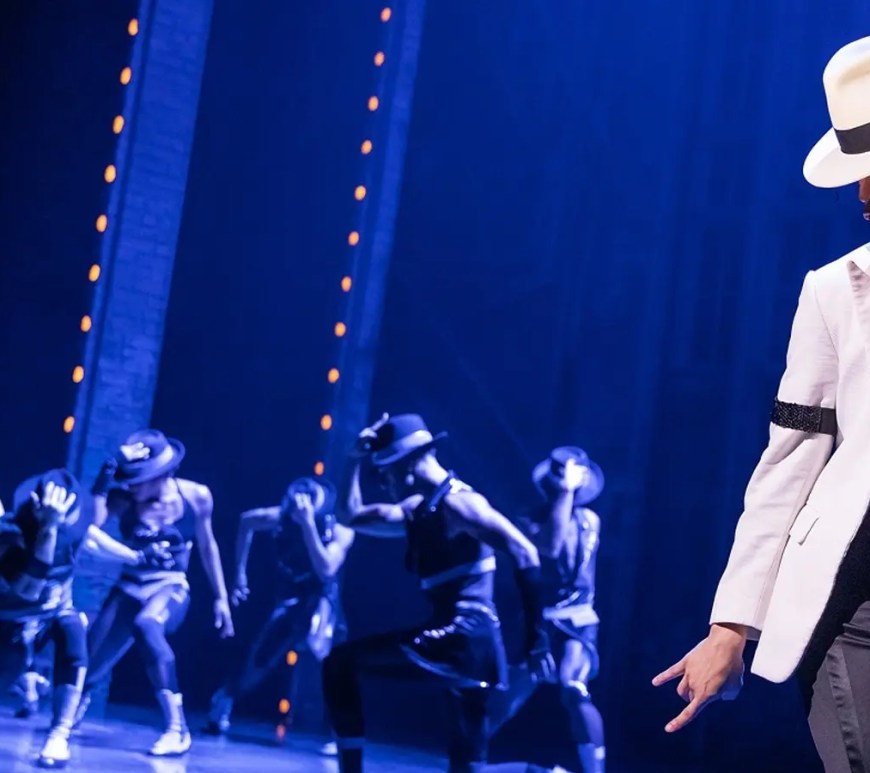 A wide-angle view of the MJ The Musical stage production at the Neil Simon Theatre, showcasing the industrial scaffolding, high-intensity theatrical lighting, and the 1990s rehearsal studio aesthetic.