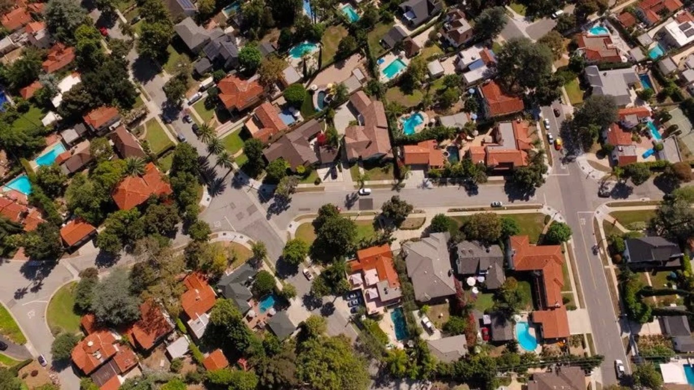 A quiet American suburban neighborhood with tree‑lined streets and rows of single‑family homes under soft daylight, representing the traditional image of the American Dream.
