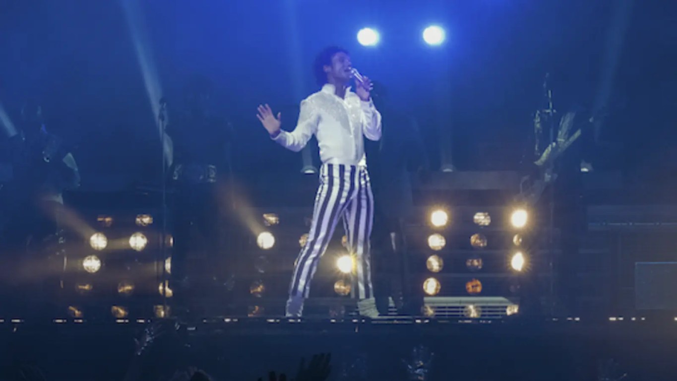 A high-definition official movie still from the 2026 biopic ‘Michael’ featuring Jaafar Jackson as Michael Jackson, performing on stage in a cinematic 65mm Panavision frame that captures the scale of the King of Pop’s stadium era, currently headlining today’s historic April 22nd Early Access ticket drop.