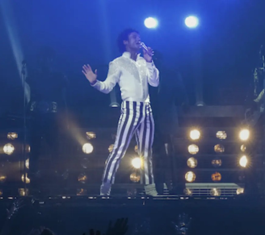 A high-definition official movie still from the 2026 biopic ‘Michael’ featuring Jaafar Jackson as Michael Jackson, performing on stage in a cinematic 65mm Panavision frame that captures the scale of the King of Pop’s stadium era, currently headlining today’s historic April 22nd Early Access ticket drop.