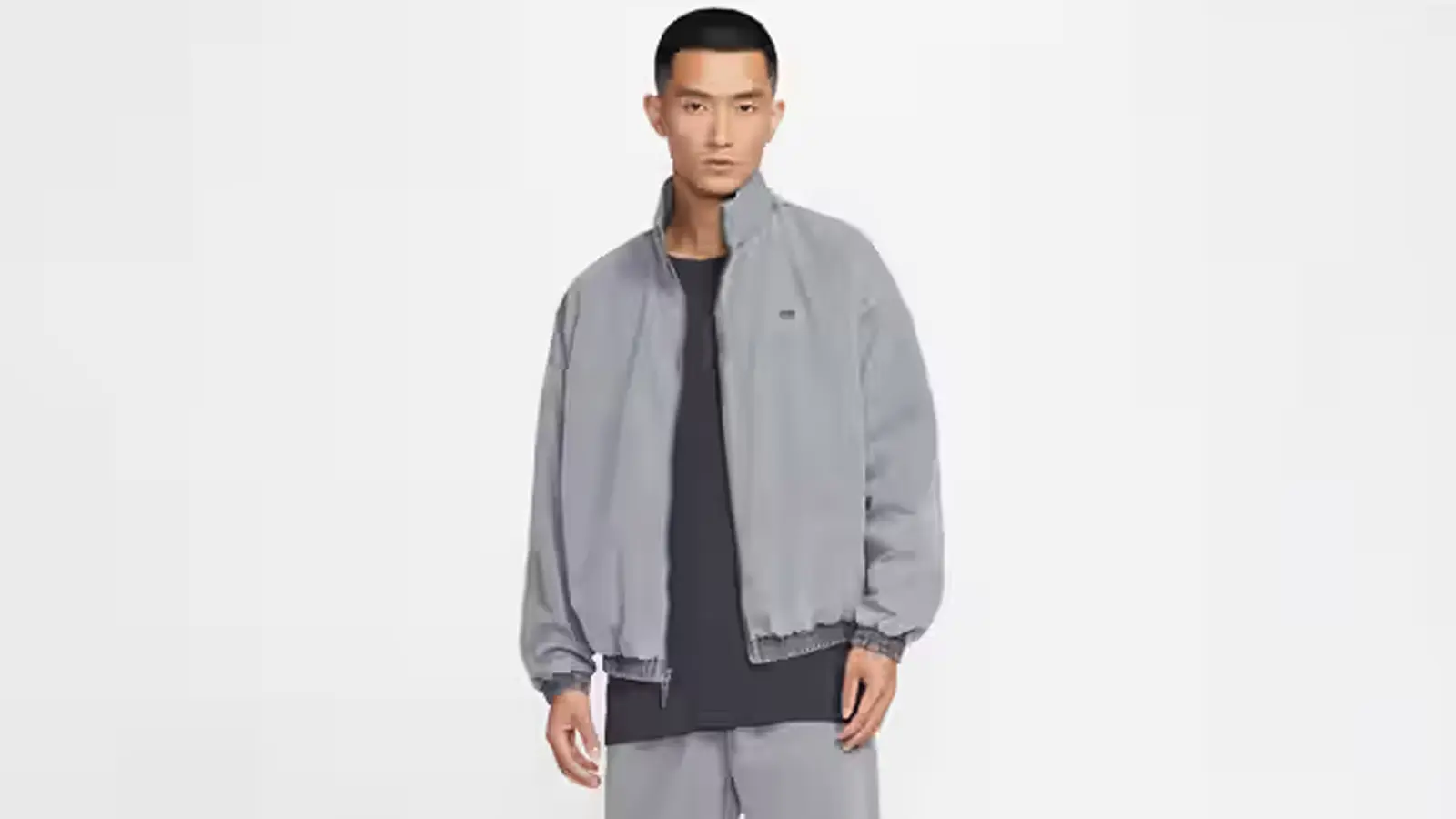 A studio profile of the Nike Book 'Chapter II' Woven Game Jacket in both Black and Tattoo colorways, showcasing the sun-faded dye finish, Dri-FIT woven fabric, and relaxed fit.