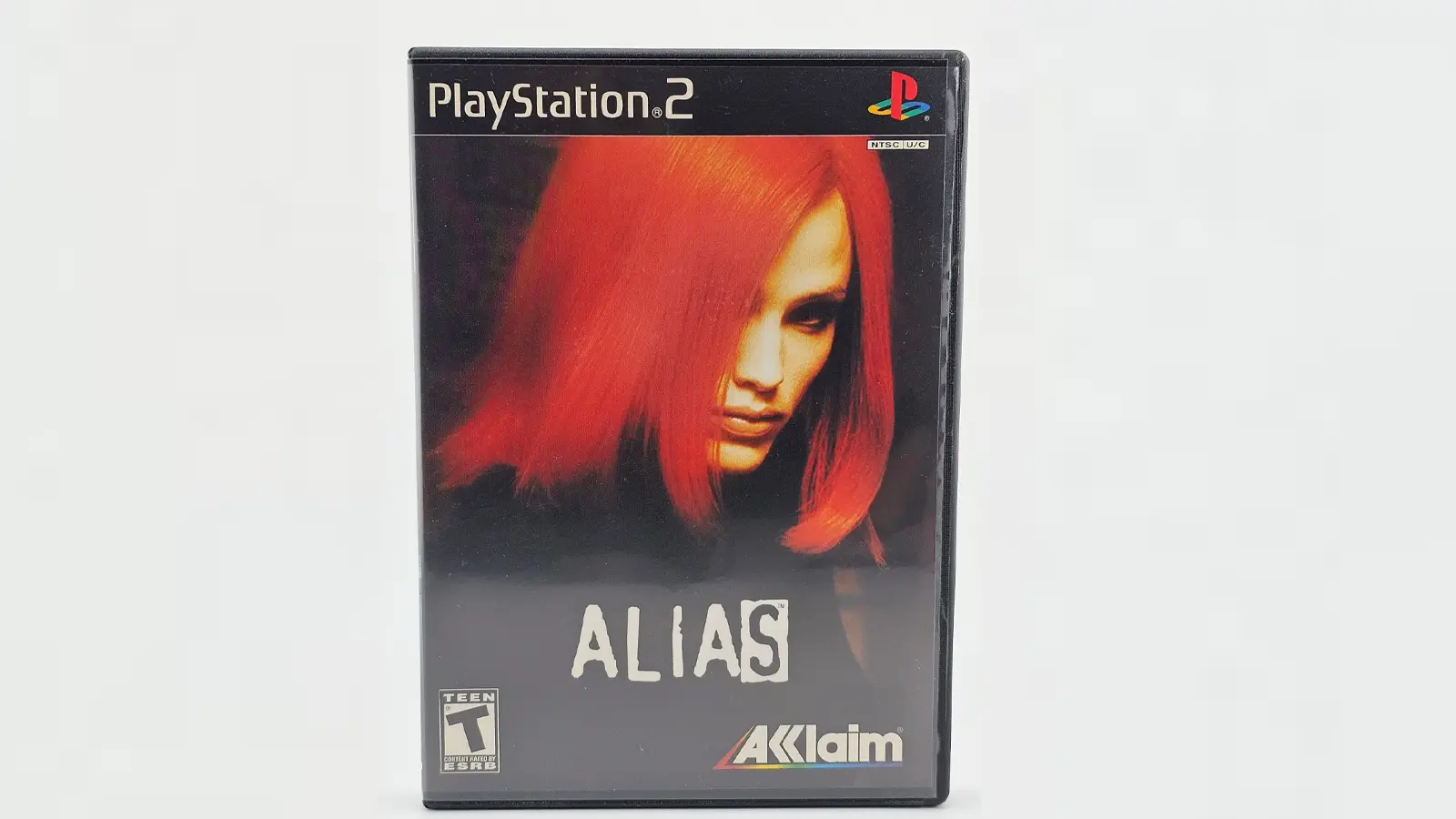 The official cover art for the 2004 Alias video game, featuring Jennifer Garner as Sydney Bristow. She is positioned in a dynamic 'hero pose' in the center, wearing her iconic black tactical stealth suit and holding a high-tech gadget. The background features a digital 'Rambaldi' clock interface and a high-contrast blue and black color palette, with the PlayStation 2 and Acclaim logos visible at the bottom.