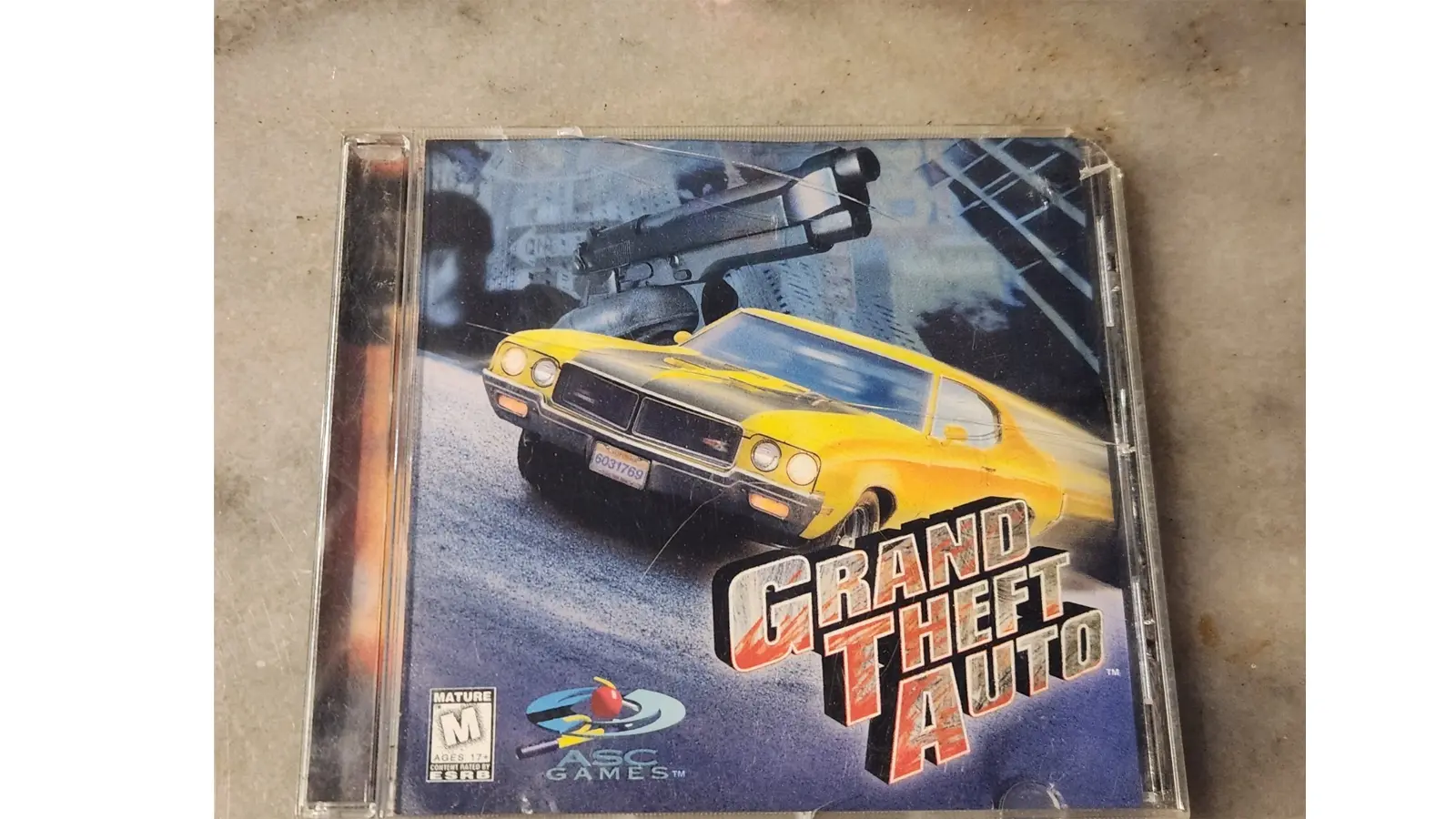 The original 1997 Grand Theft Auto PC big-box art featuring a fisheye lens photograph of the NYC skyline with a yellow taxi and a red car in the foreground. The logo is stacked in three levels with a yellow-to-orange gradient, bold black outlines, wanted stars, and a stylized flame emerging from the center.