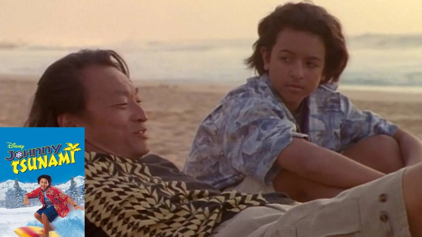 Brandon Baker as Johnny Kapahala standing with a surfboard on a Hawaiian beach in Johnny Tsunami (1999)