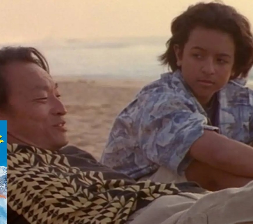 Brandon Baker as Johnny Kapahala standing with a surfboard on a Hawaiian beach in Johnny Tsunami (1999)