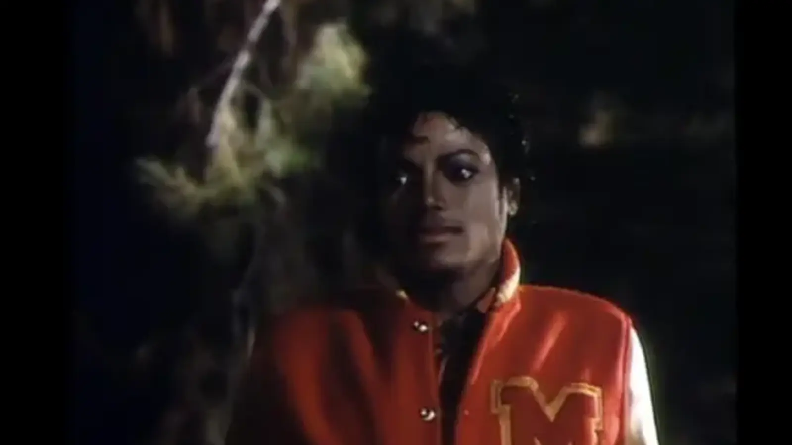 Michael Jackson wearing the red and yellow 'M' varsity jacket in the 1983 Thriller music video, highlighting the leather sleeves and wool body construction.