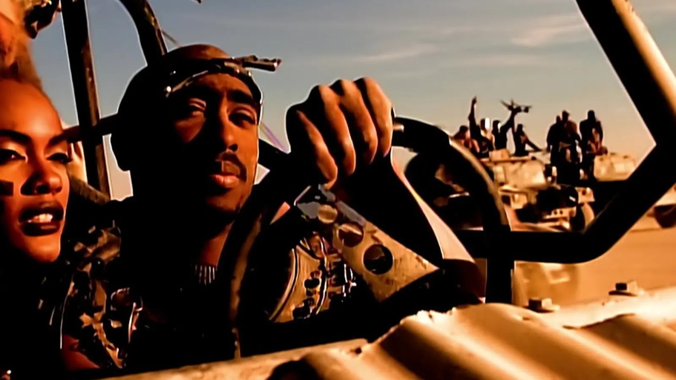 Tupac Shakur and Dr. Dre performing inside the custom steel 'Thunderdome' set in the El Mirage desert, showcasing the high-budget visual engineering of the California Love music video.