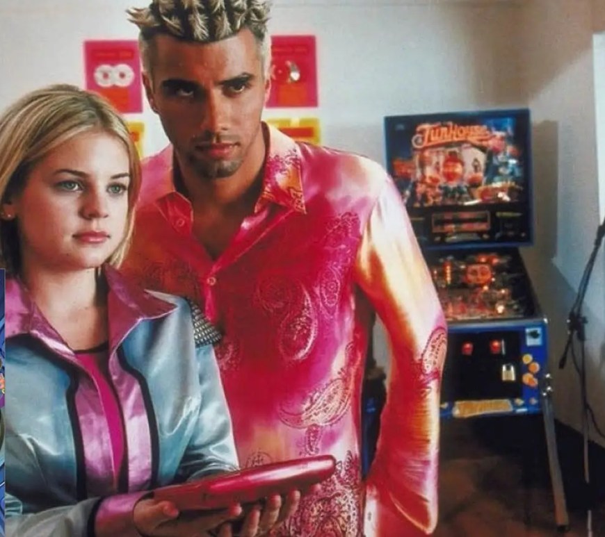 Kirsten Storms as Zenon Kar and Shadia Simmons as Nebula Wade in their metallic 2001 'Zequel' outfits, looking at a Zap-Pad in the Alien Patrol lab.