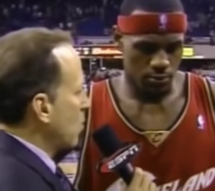 LeBron James, aged 18, being interviewed by ESPN’s Jim Gray at ARCO Arena following his NBA debut on October 29, 2003. James is wearing his wine-and-gold Cleveland Cavaliers road jersey, appearing calm despite the 106-92 loss to the Sacramento Kings.