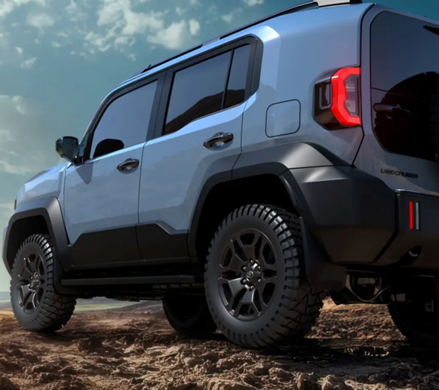 The 2026 Toyota Land Cruiser FJ in Heritage Blue, showing the retro boxy silhouette and round LED headlights in an off-road mountain setting.