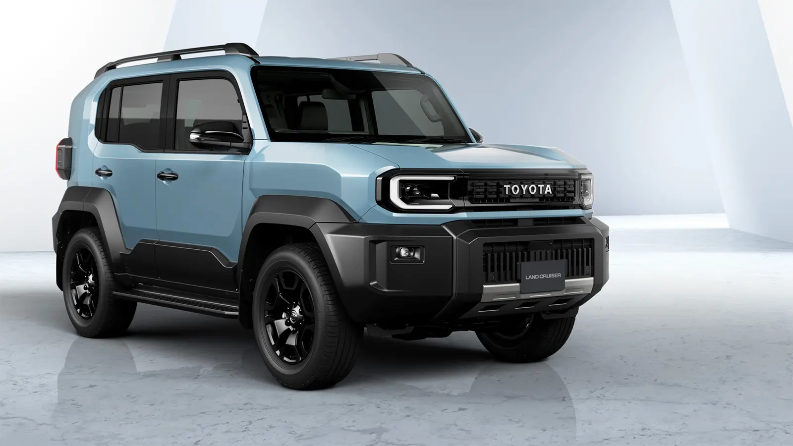 The 2026 Toyota Land Cruiser FJ in Heritage Blue, showing the retro boxy silhouette and round LED headlights in an off-road mountain setting.