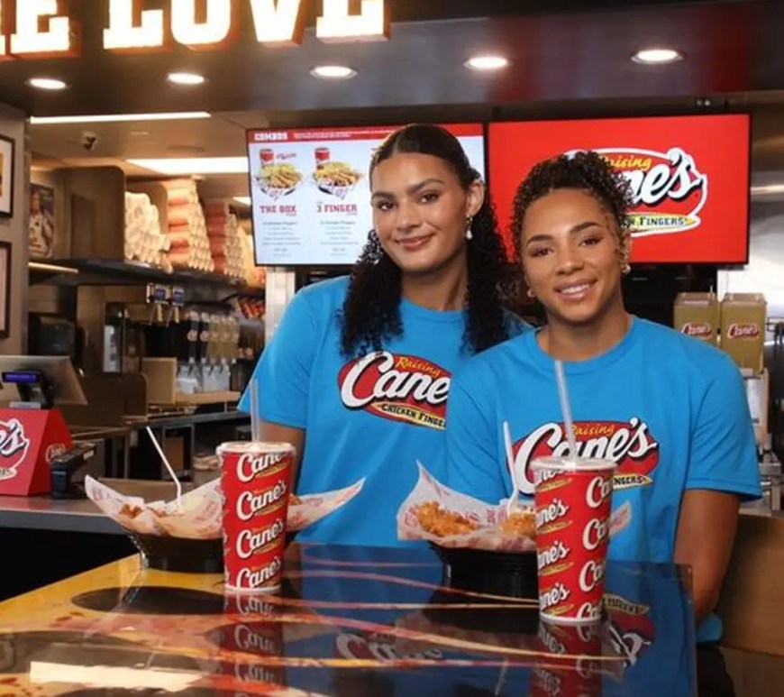 Lauren Betts and Kiki Rice in Raising Cane’s uniforms holding a Box Combo and a basketball in Hollywood.