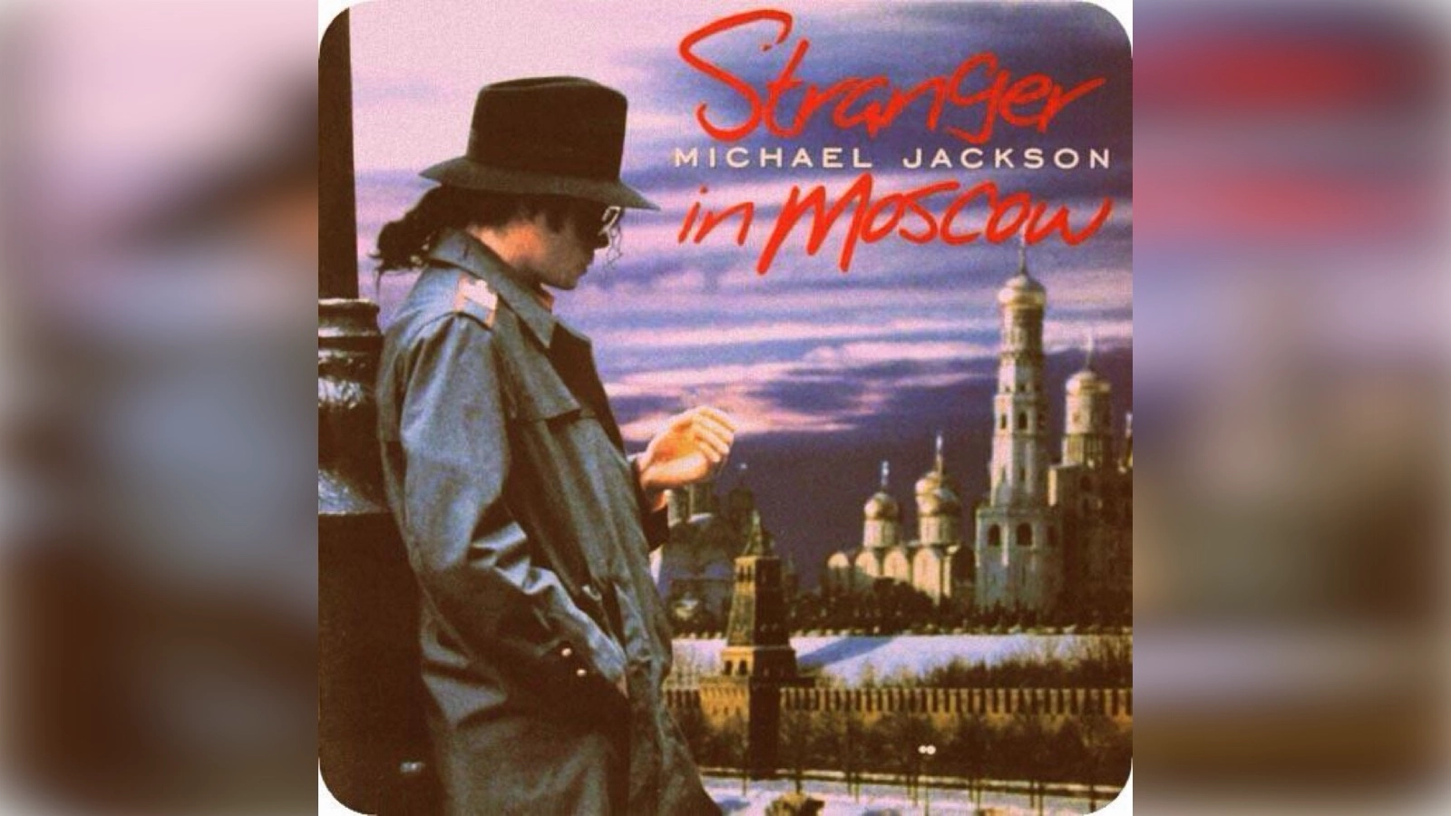 Michael Jackson stands in profile wearing a dark trench coat and hat against a moody Moscow skyline with onion‑domed architecture, under twilight skies, with the title ‘Stranger in Moscow’ above him.