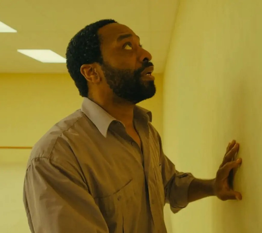 A wide cinematic promotional still from Backrooms showcasing massive, practical yellow office set.