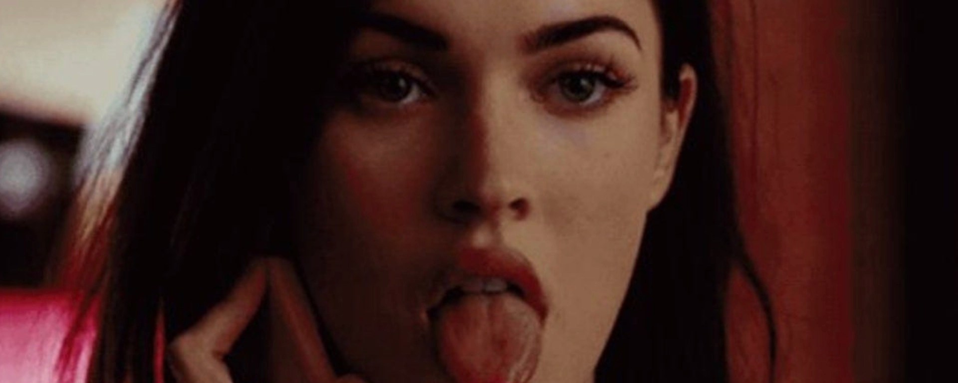 Close-up cinematic still of Megan Fox in Jennifer's Body holding a lit silver lighter directly to her tongue, showcasing the famous supernatural horror scene.