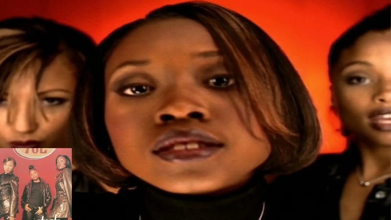 A vintage promotional photograph from the 1996 music video for 702's 'Steelo', showcasing Kameelah Williams, Irish Grinstead, and LeMisha Grinstead in classic mid-90s streetwear.