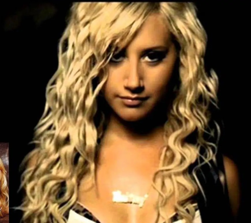 A bright, early-2000s styled music video film still of Ashley Tisdale performing with dancers under vibrant club staging lights.