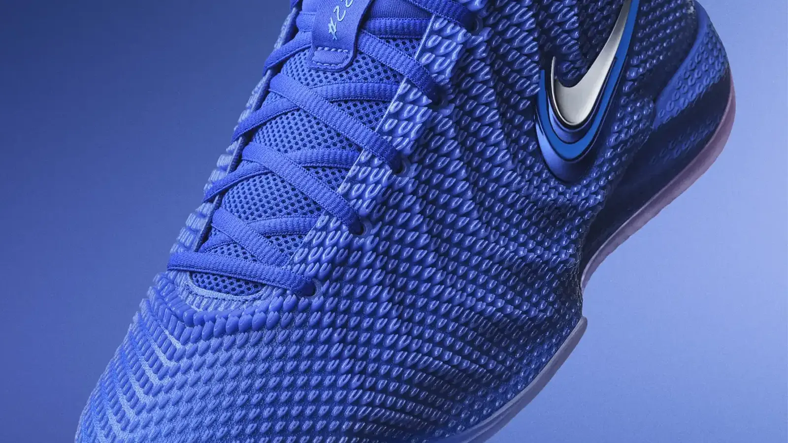A side-profile studio photograph of the Nike Caitlin 1 basketball shoe in the "Racer Blue" colorway. The design features a low-top silhouette with a white midsole and a striking royal blue upper covered in textured, wave-like polyurethane nodes that form a distinct ripple pattern.