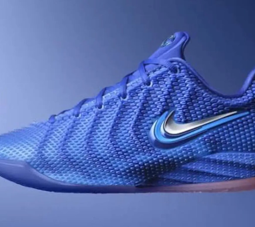 A side-profile studio photograph of the Nike Caitlin 1 basketball shoe in the "Racer Blue" colorway. The design features a low-top silhouette with a white midsole and a striking royal blue upper covered in textured, wave-like polyurethane nodes that form a distinct ripple pattern.