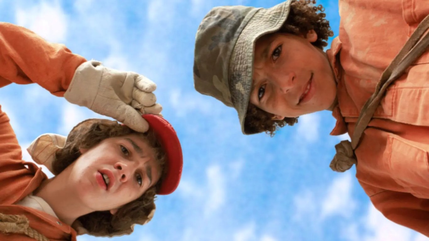 A vibrant high-contrast production still from 2003 showing Stanley Yelnats and Zero resting inside a deep dirt hole in the middle of a vast, sun-baked desert landscape.