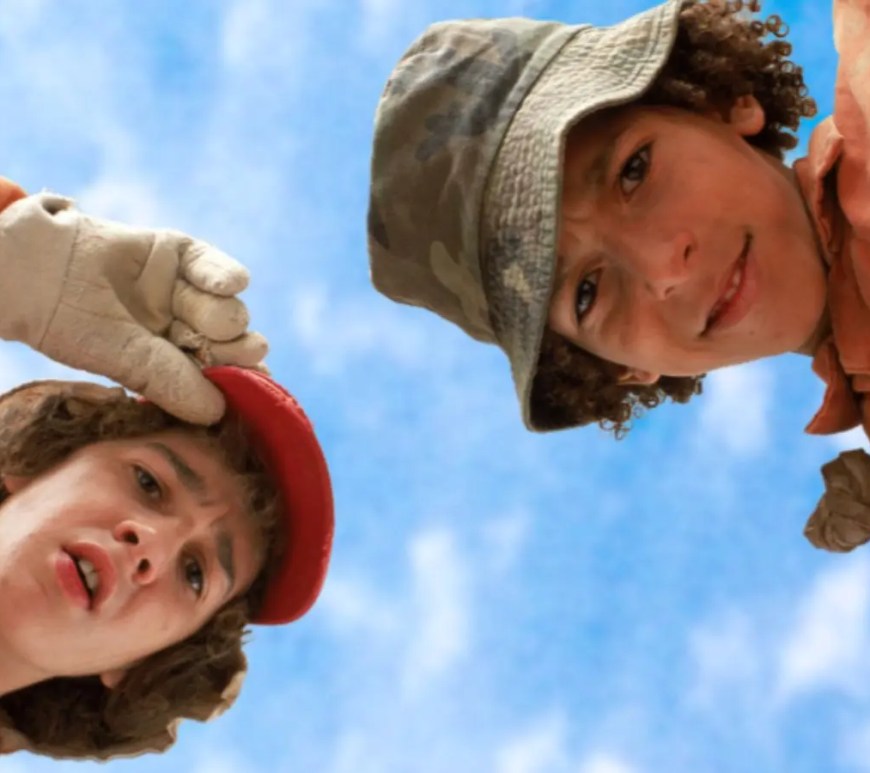 A vibrant high-contrast production still from 2003 showing Stanley Yelnats and Zero resting inside a deep dirt hole in the middle of a vast, sun-baked desert landscape.