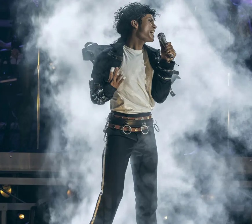A high-contrast cinematic stage performance film still from the 2026 movie Michael, showcasing Jaafar Jackson executing signature Michael Jackson choreography under bright spotlights.