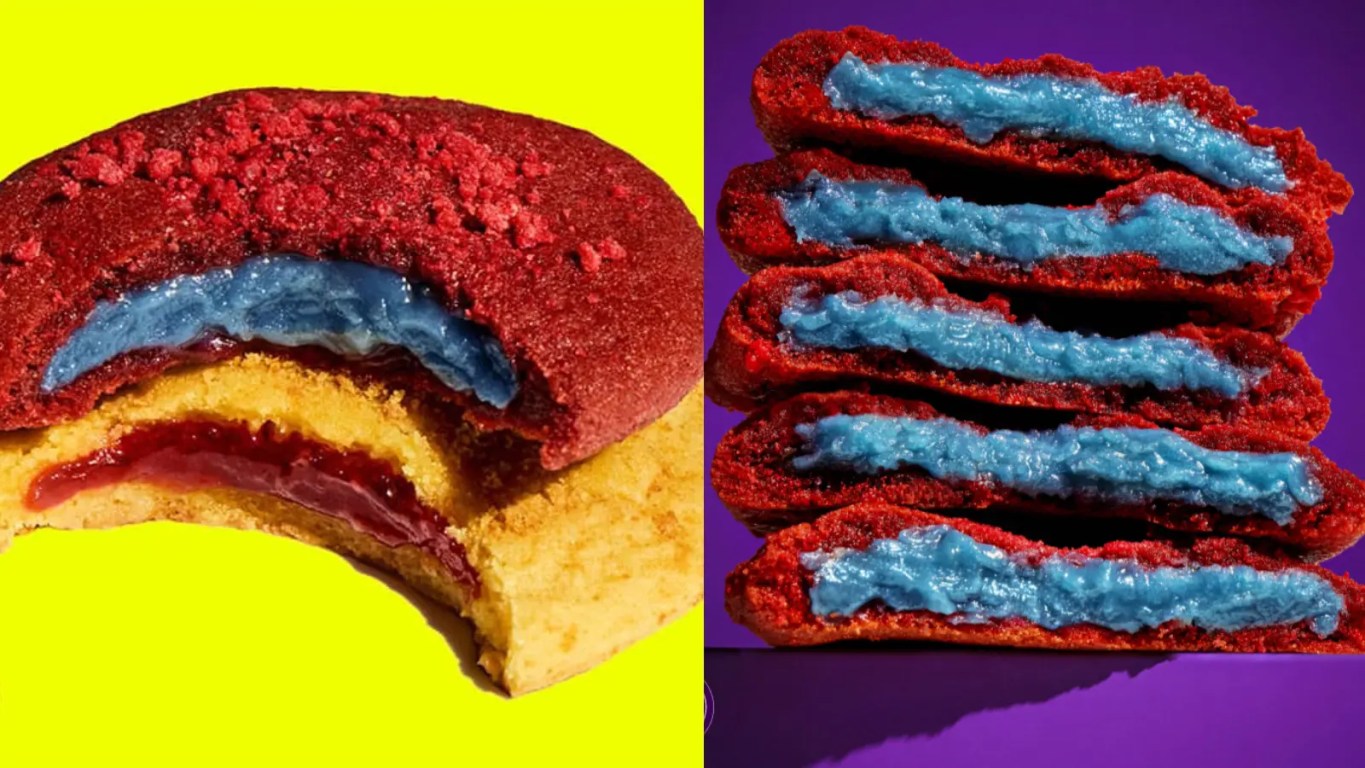 A wide close-up display showcasing promotional Insomnia Cookies packaging styled with vibrant Supergirl branding and custom movie artwork alongside newly released red velvet and lemon cookies.