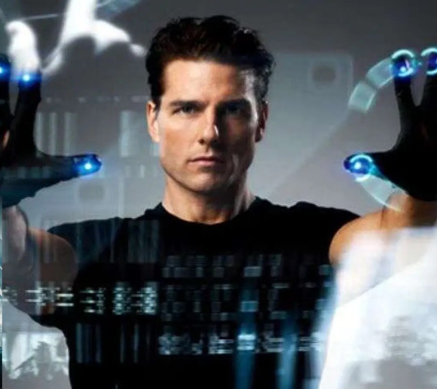 A iconic cinematic film still from the 2002 movie Minority Report, showing Tom Cruise as John Anderton using illuminated gesture-control gloves to manipulate transparent floating screens.