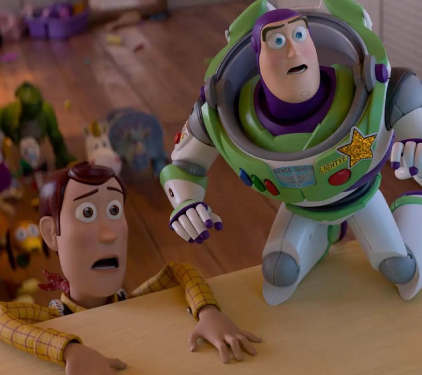 A theatrical film still from the movie showing animated characters Buzz Lightyear and Sheriff Woody standing side-by-side inside a brightly lit playroom setting.