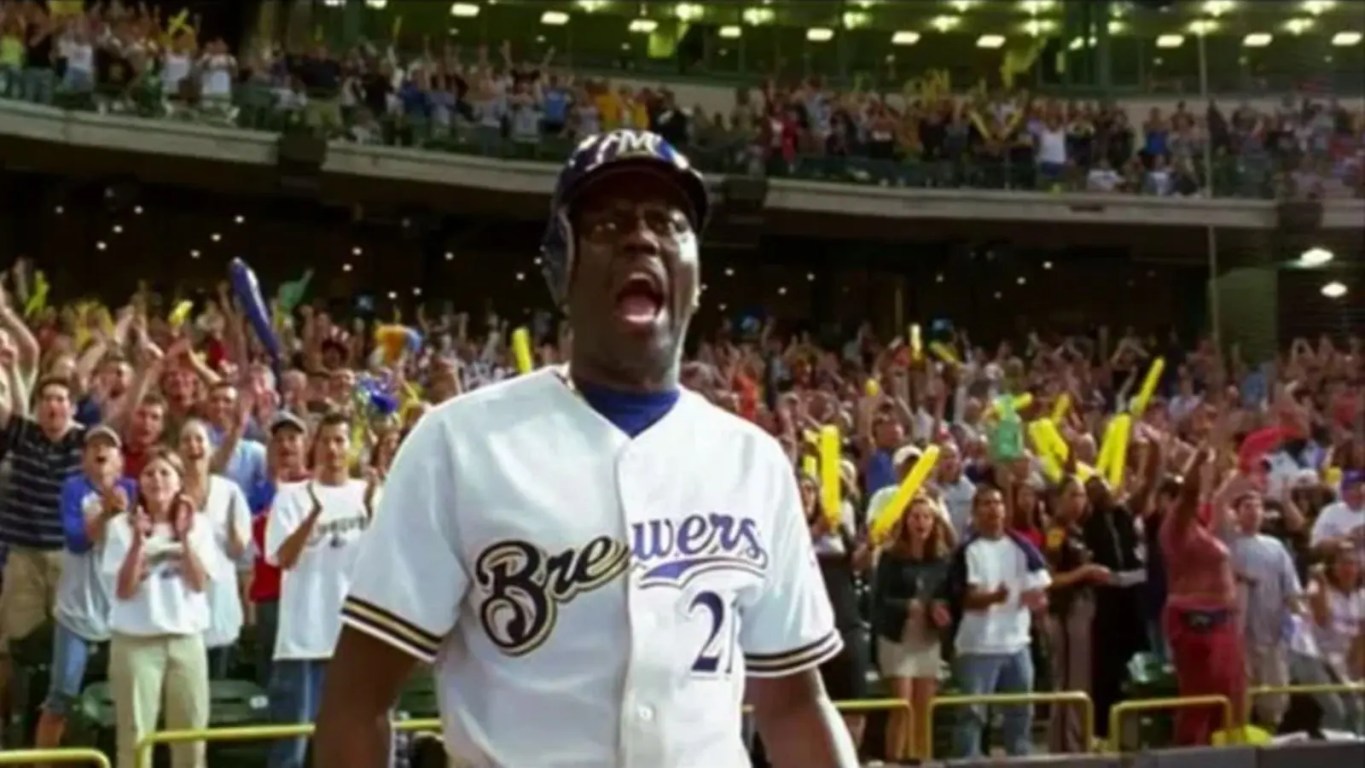 A sharp horizontal film still from the 2004 movie Mr. 3000 showing Bernie Mac in a crisp white and navy Milwaukee Brewers uniform pointing confidently from the batter's box.