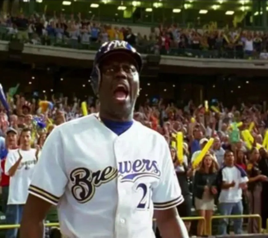 A sharp horizontal film still from the 2004 movie Mr. 3000 showing Bernie Mac in a crisp white and navy Milwaukee Brewers uniform pointing confidently from the batter's box.